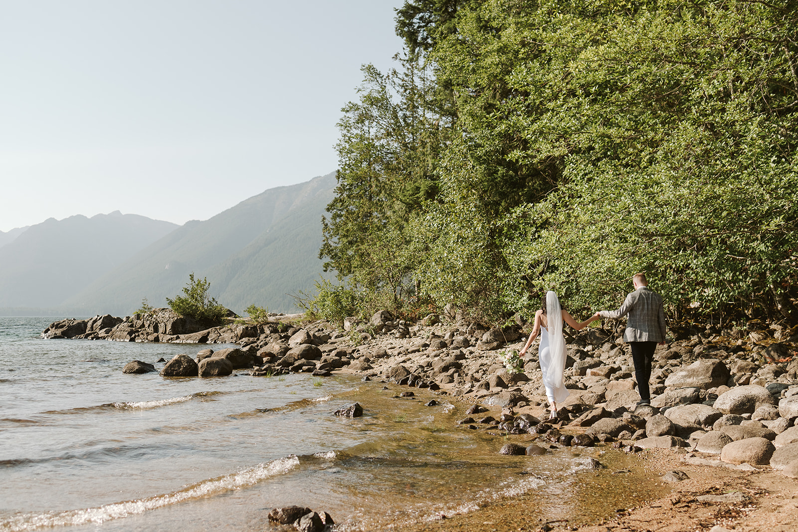 Newlyweds walk along lake edge