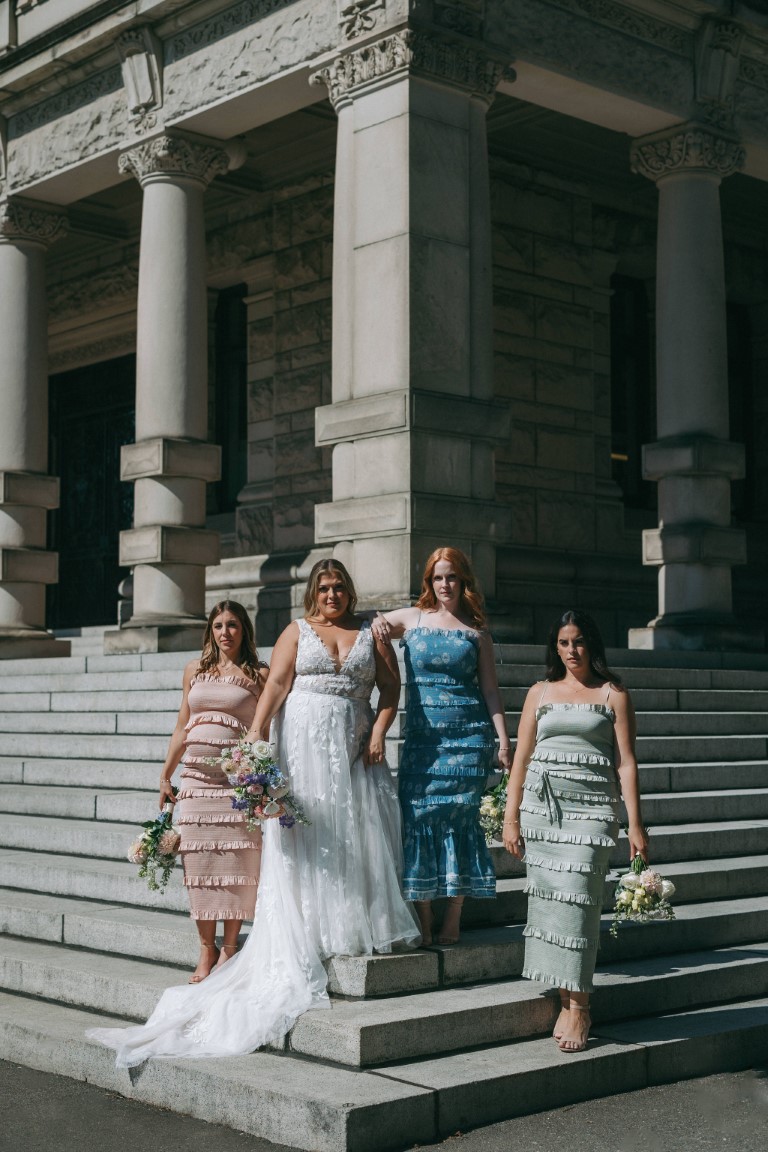 Bride and bridesmaids in rainbow colors stand on Parliament steps