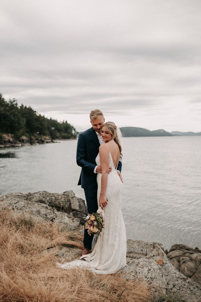 Newlyweds pose in front of ocean view at Poets Cove