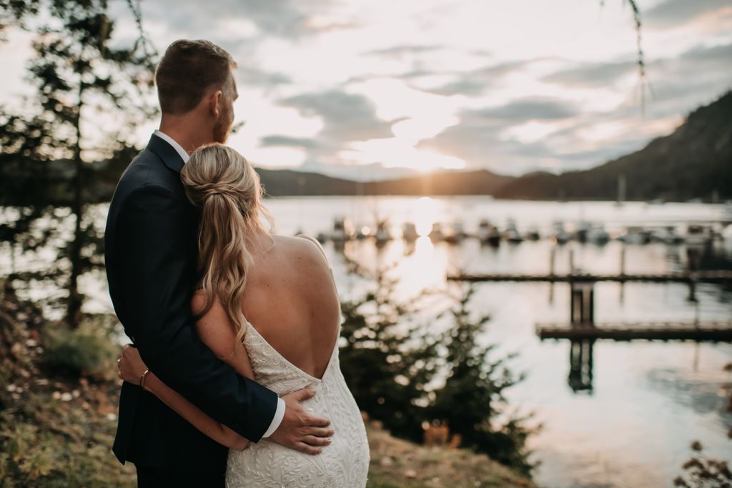 Bride and groom hug while watching sunset at Poet's Cove