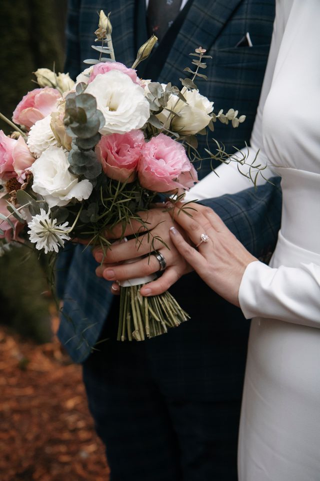 Bride and groom clasp white and pink peony bouquet