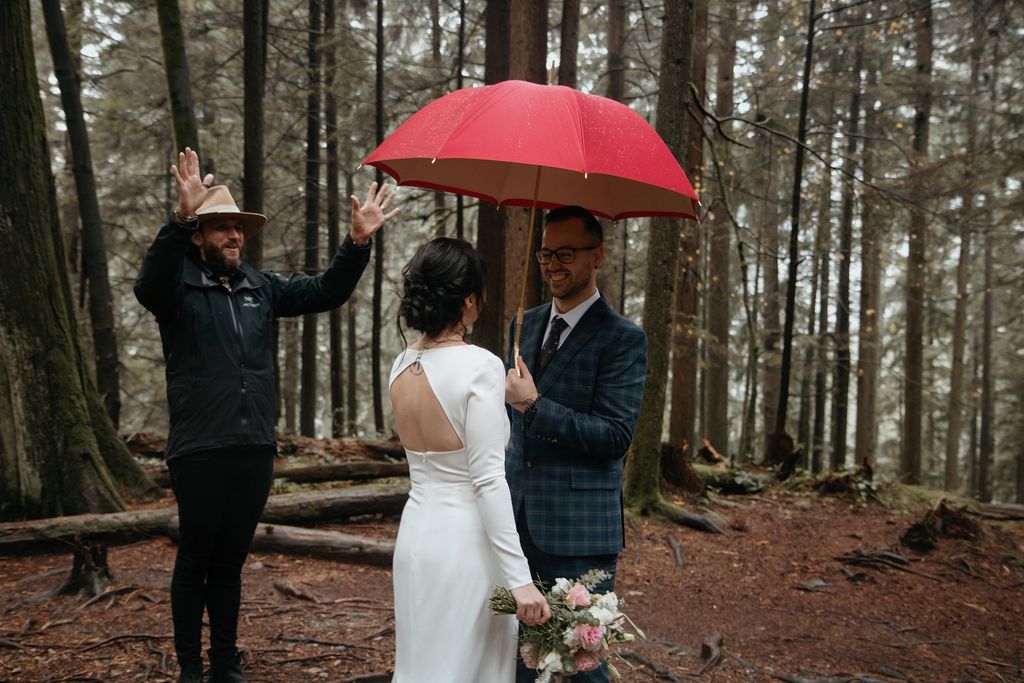 Bride and groom exchange vows in rainforest under red umbrella