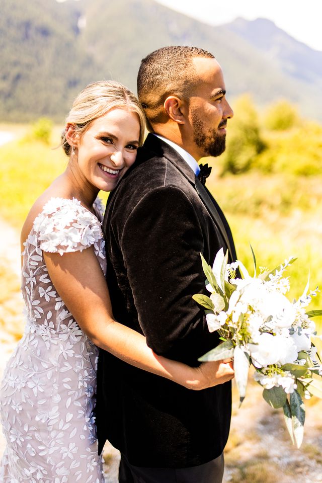 Bride leans on grooms back with bouquet