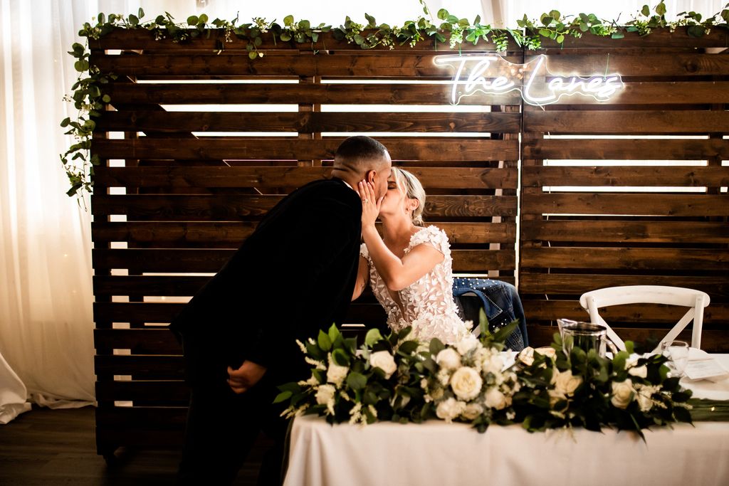 Newlyweds kiss at sweetheart table with wood backdrop