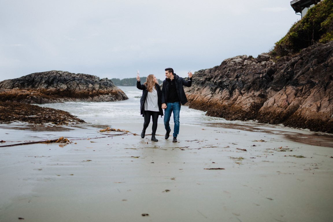 Engaged couple walk along Tofino beach