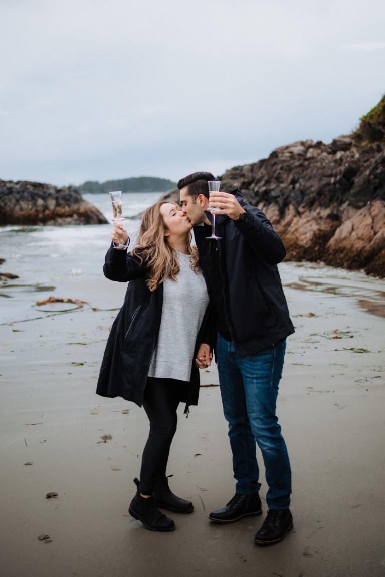 Engaged couple kiss and toast on Tofino beach