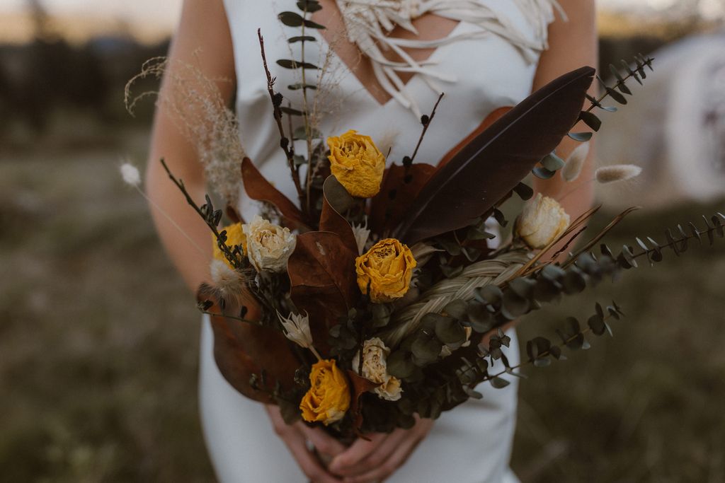 Indigenous bride holds yellow and red bouquet with feather