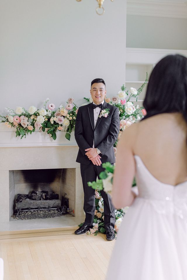 Groom waits for bride in front of white fireplace