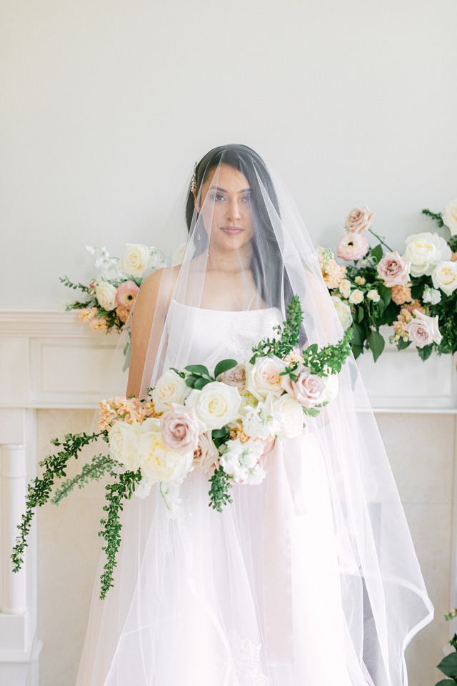 Bride in blusher veil sits in front of white fireplace