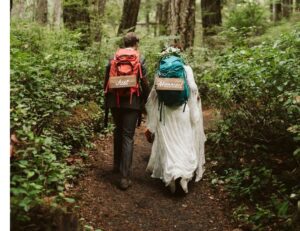 Newlyweds backpack on forest path by Aly Sibley