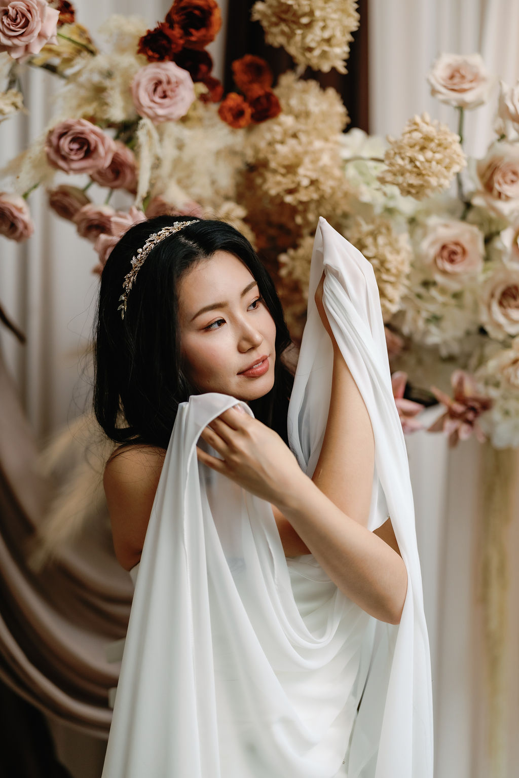 bride holds draped gown in front of beige hydrangeas